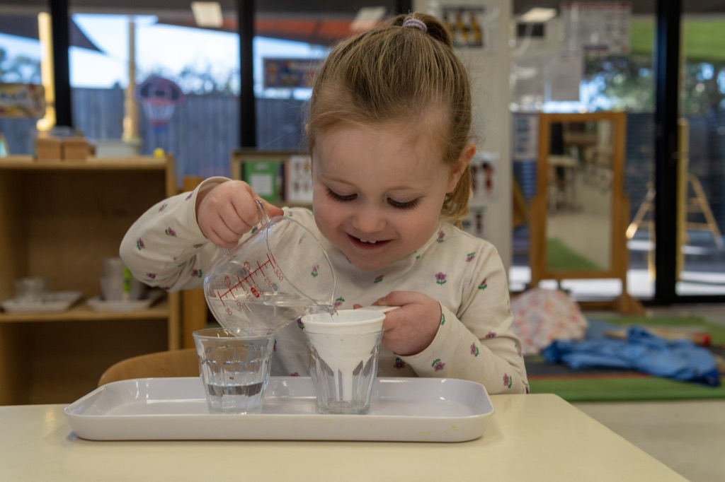 A child pouring water between glasses in a practical life activity