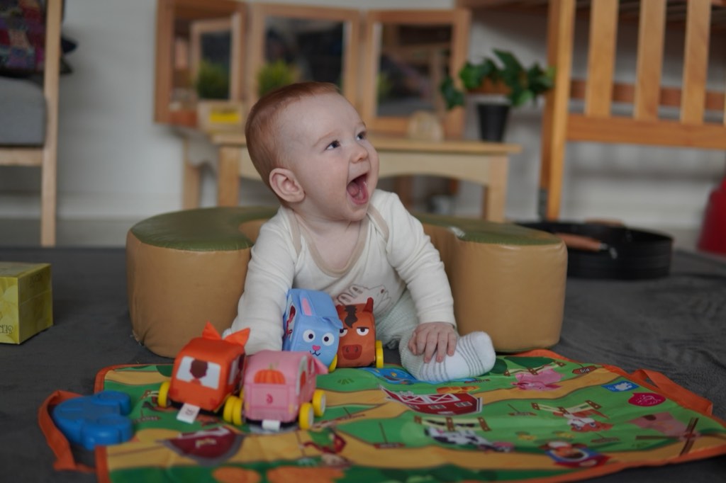 A laughing baby playing with soft cars in the Billy-beet Melton infant room
