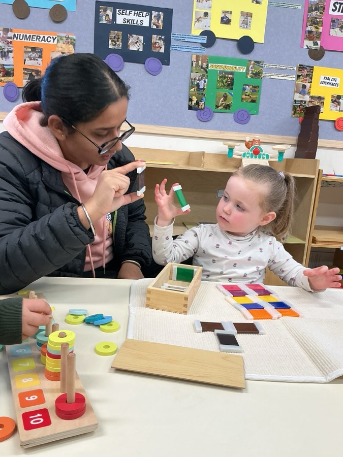 An educator presenting Montessori colour tablets and knobbed cylinders to a child